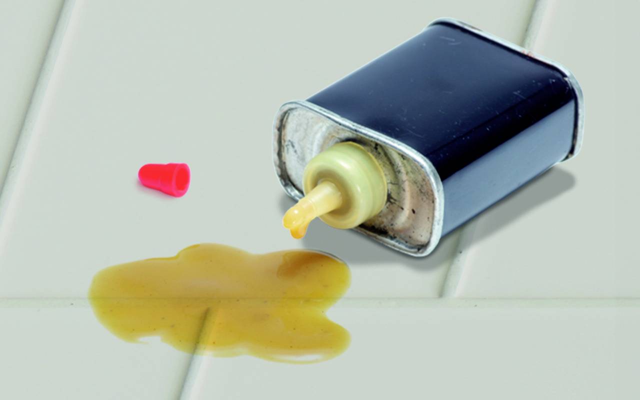 Przewrócona puszka z rozlanym żółtym płynnym klejem na stole. Obok leży czerwona nakrętka.