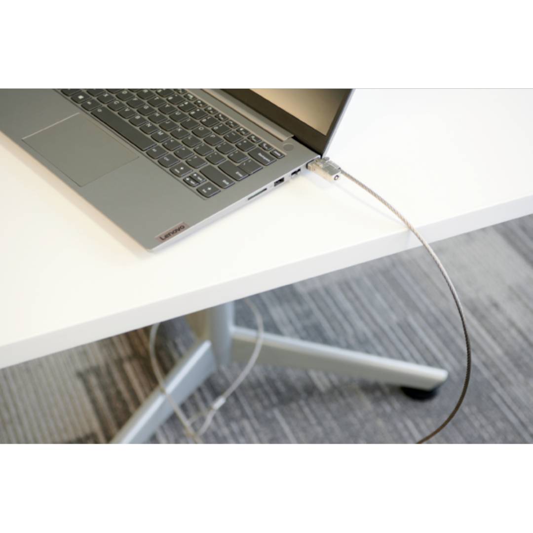 Szary laptop leży na białym stole. Kabel zabezpieczający jest przymocowany do boku laptopa i zabezpiecza go przed kradzieżą.