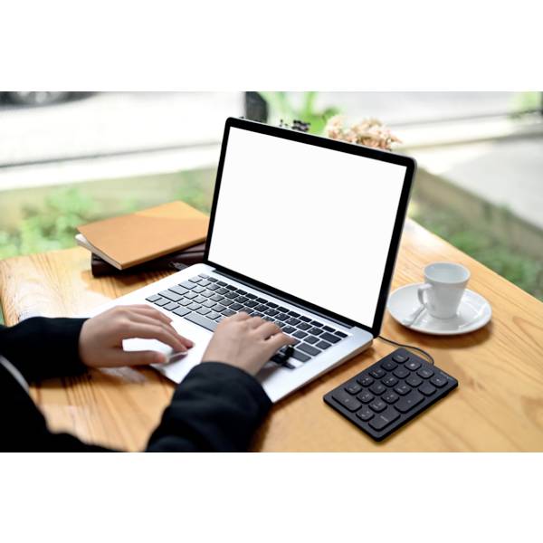 Osoba pracuje na laptopie przy drewnianym stole, obok której leży notes, filiżanka kawy i kalkulator.