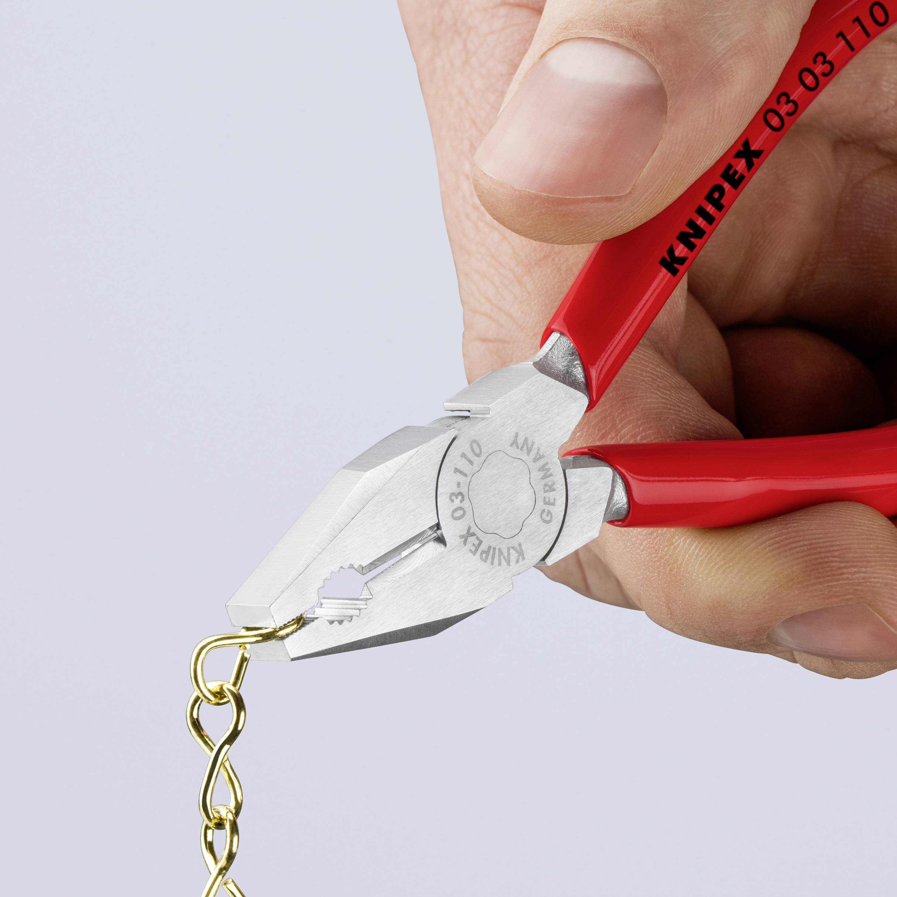 Ręka trzyma czerwone szczypce marki Knipex, które przecinają małą łańcuszek.