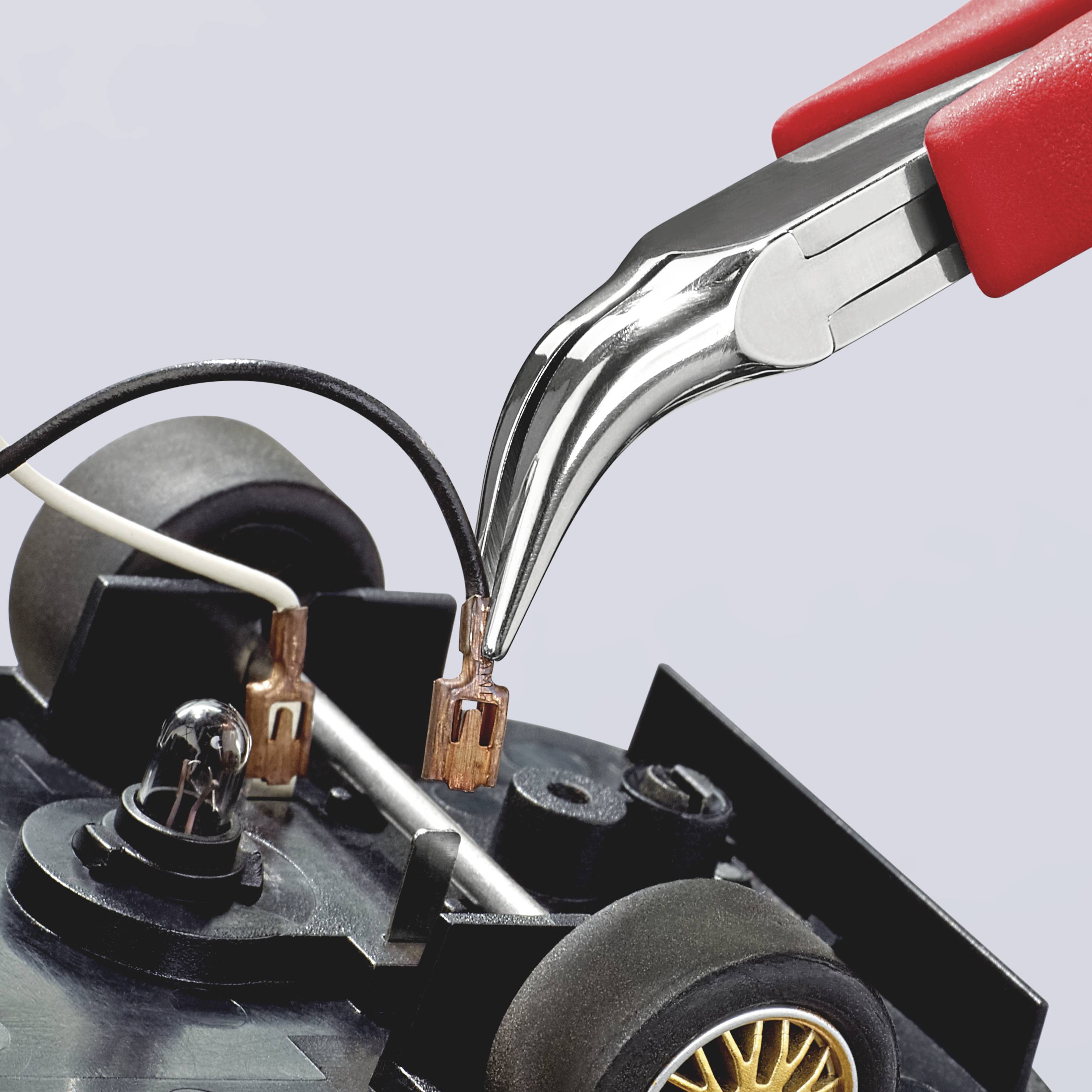 Zbliżenie czerwonych szczypiec trzymających małą część elektroniczną na płycie głównej. W tle widoczne są przewody.