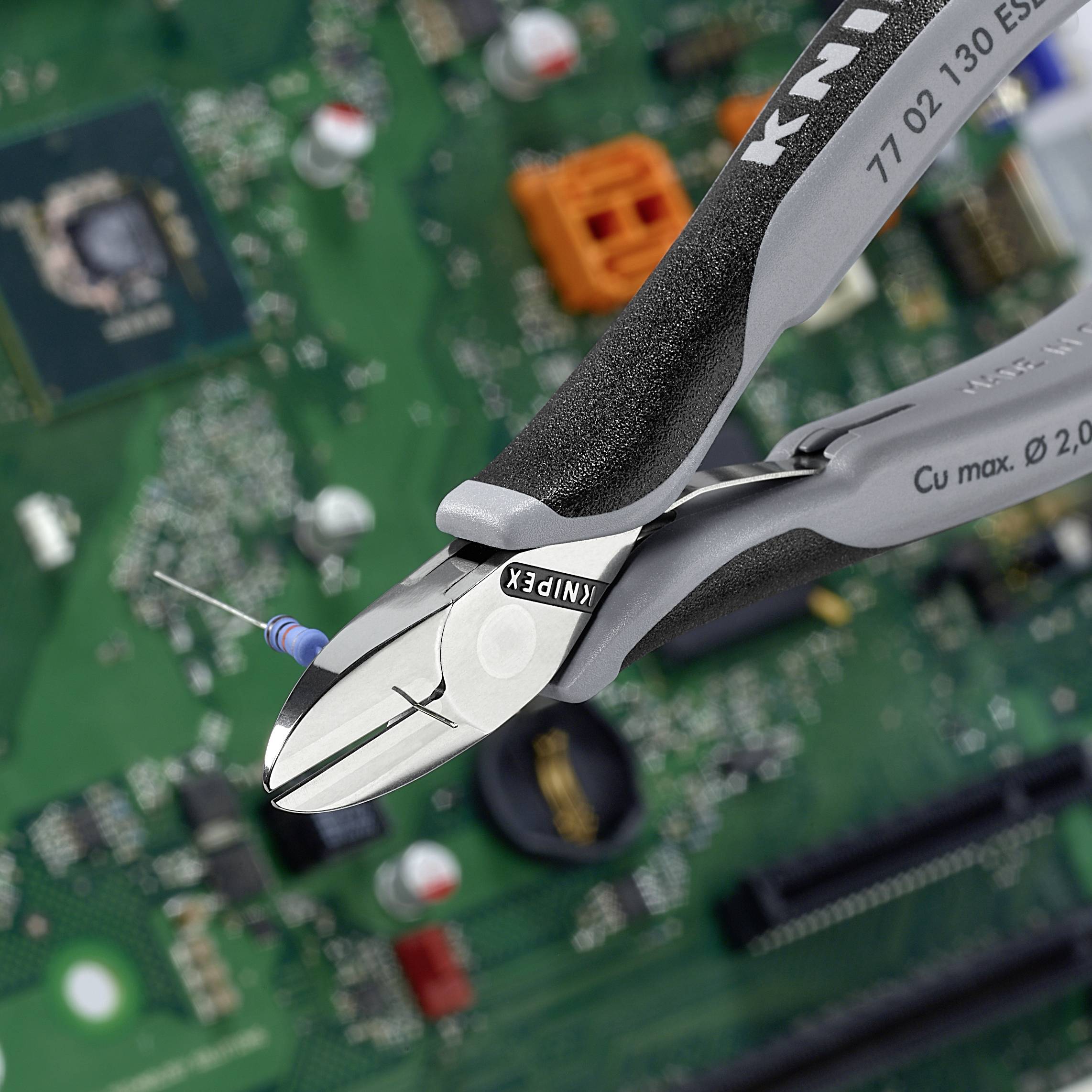 Szczypce elektroniczne przecinają przewód na płytce drukowanej. W tle widoczne są różne elementy elektroniczne.