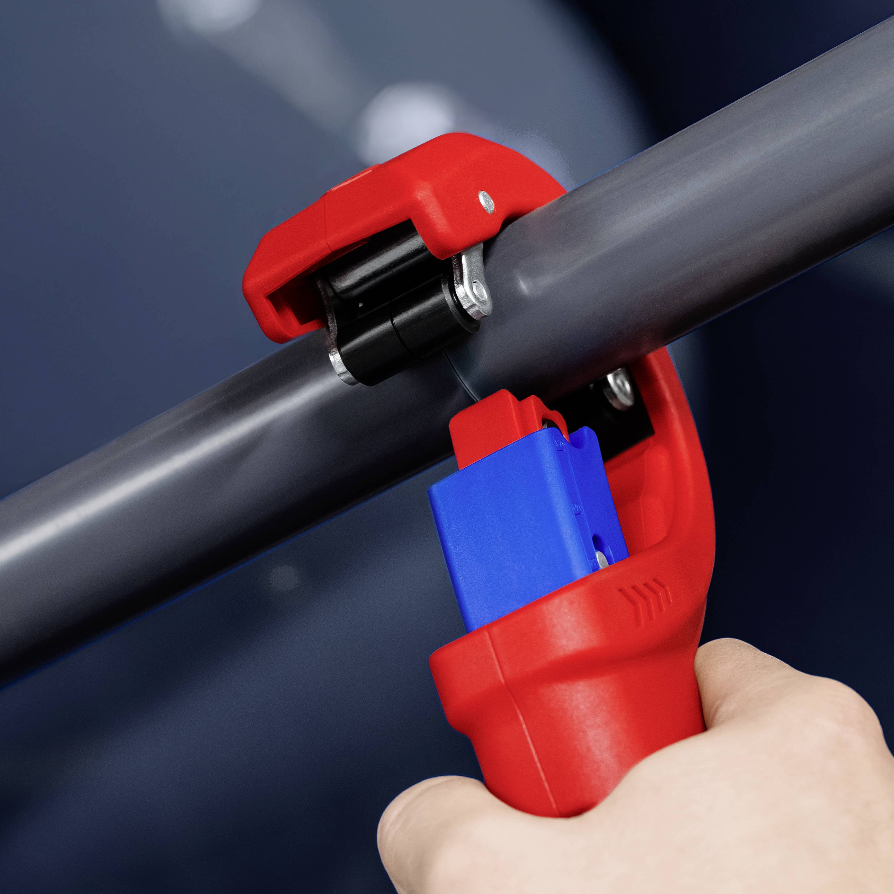 Osoba ucina szare rury za pomocą czerwonego obcinaka do rur. Fokus jest na narzędziu.