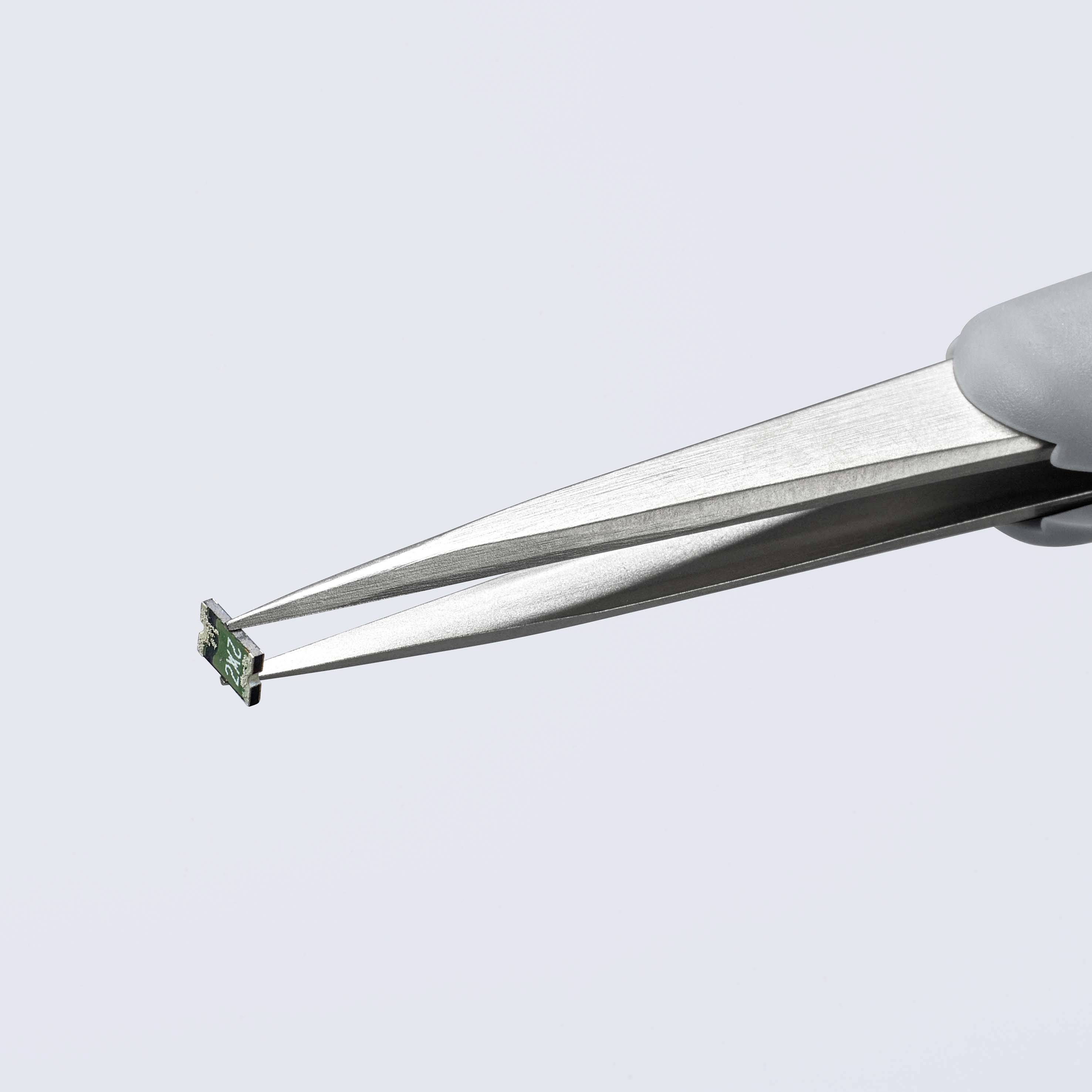 Pęseta trzyma mały zielony mikrochip, symbolizujący precyzję techniczną i mikroskopijną dokładność.