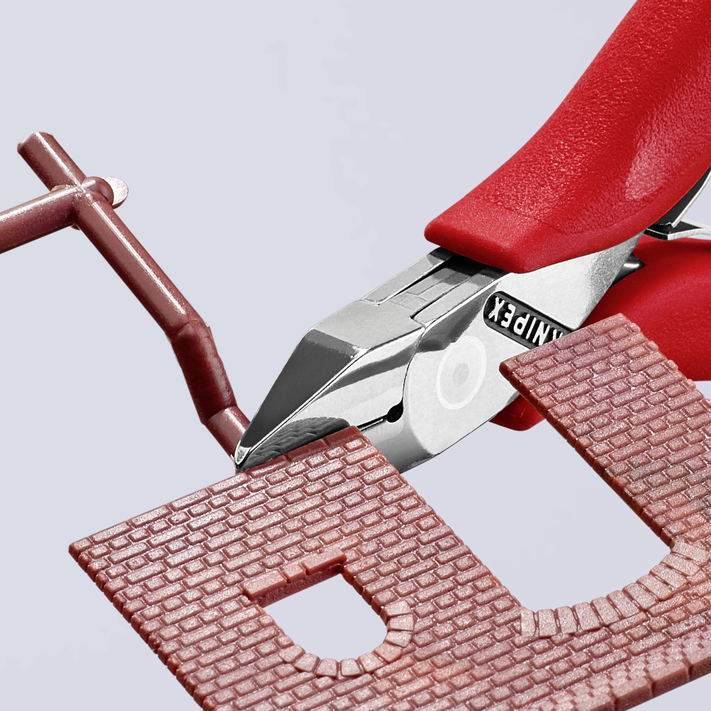 Czerwone szczypce precyzyjnie przecinają małą, kasztanowobrązową część plastikową.