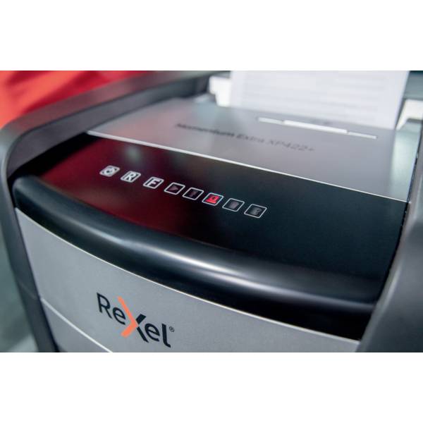 Niszczarka dokumentów marki "Rexel" napełniona papierem, która jest aktualnie włączona. Na panelu sterowania widoczne są różne symbole ustawień.