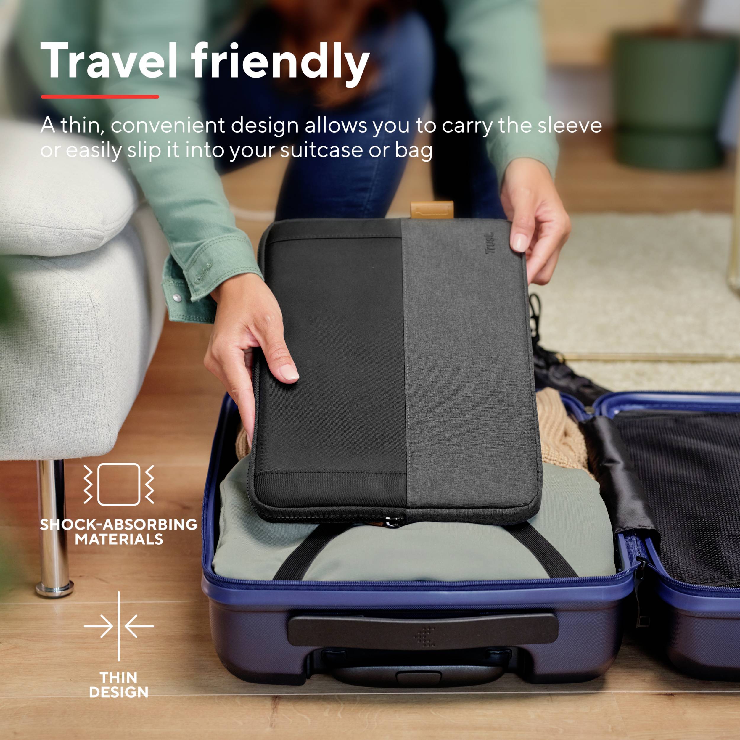 Osoba wkłada laptopa w pokrowiec do niebieskiej walizki. Tekst: 'Przyjazne podróżom' i 'Materiały pochłaniające wstrząsy'.