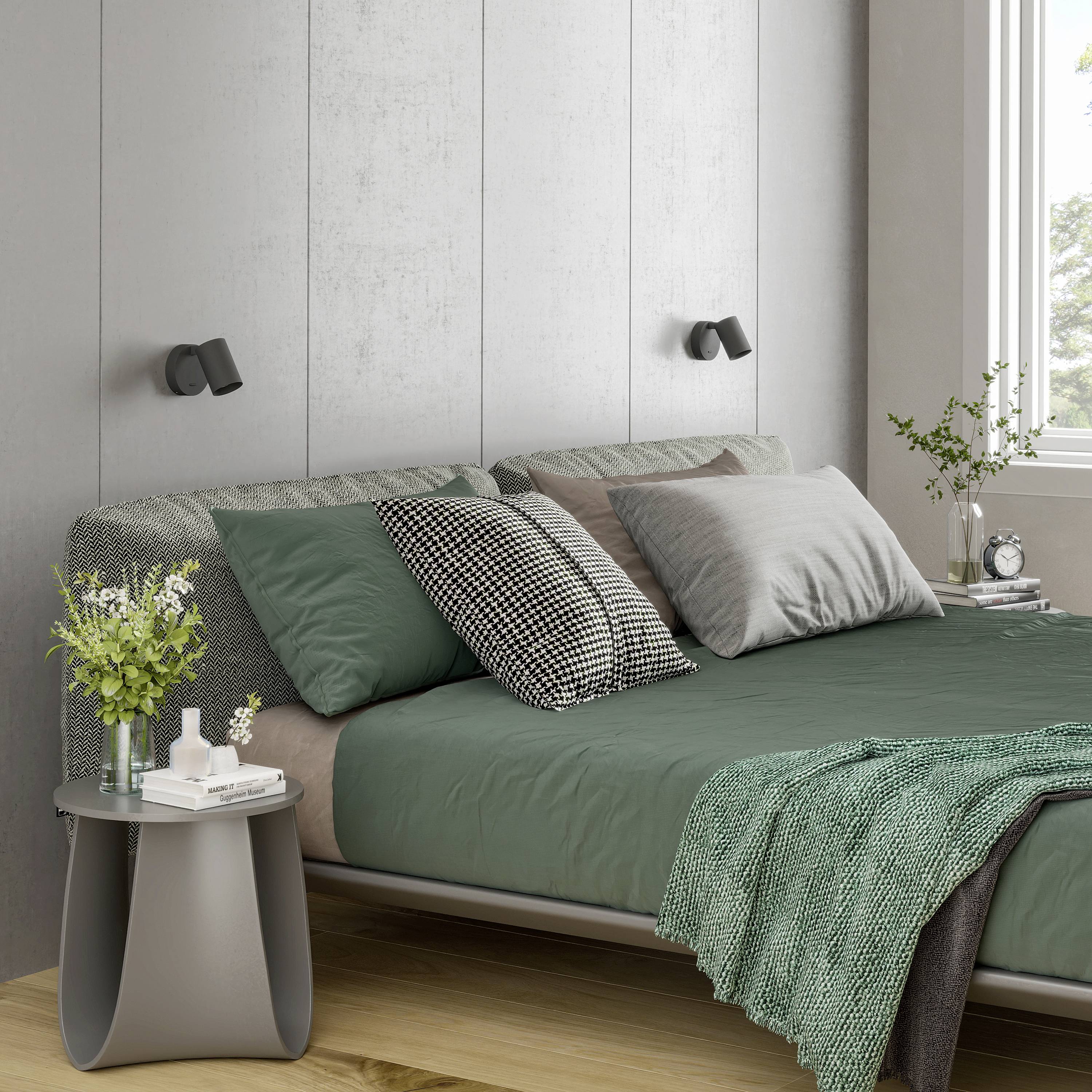 Nowoczesna sypialnia z szarą ścianą, zielonym łóżkiem i białymi poduszkami. Rośliny i stoliki nocne z lampami po lewej i prawej stronie łóżka.