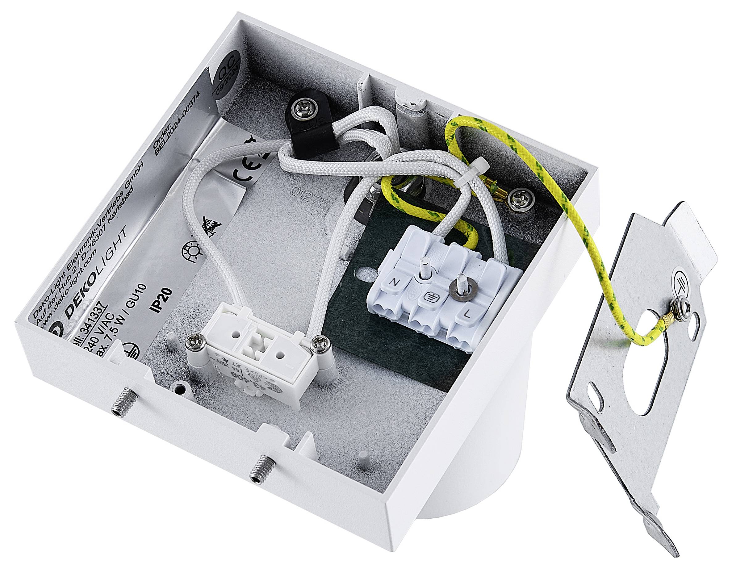 Otwarta skrzynka elektroniczna z kablami i złączami, ukazująca wewnętrzne okablowanie. Obok leży metalowy element mocujący.