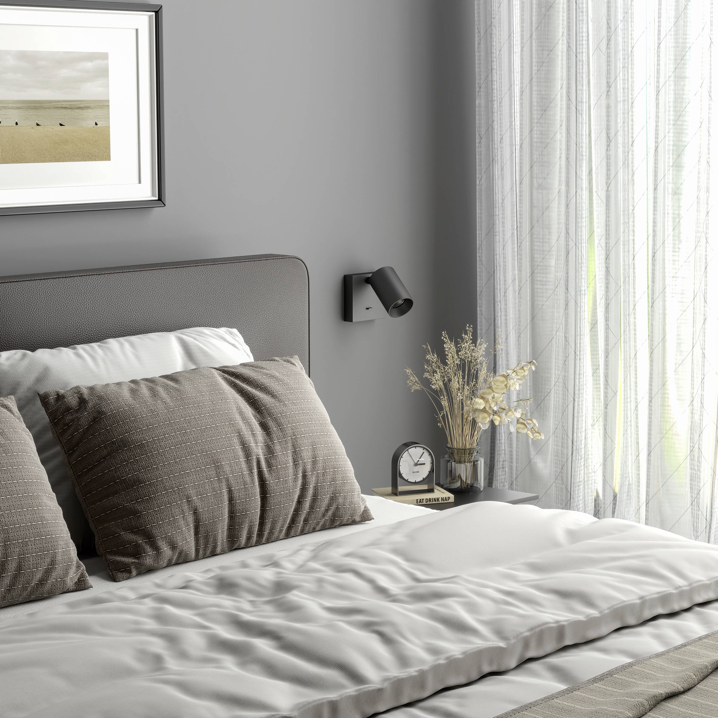 Łóżko z szarą pościelą w nowocześnie urządzonym pomieszczeniu. Na ścianie wisi obraz z krajobrazem. Na stoliku nocnym stoi lampa i ozdobny kwiat.