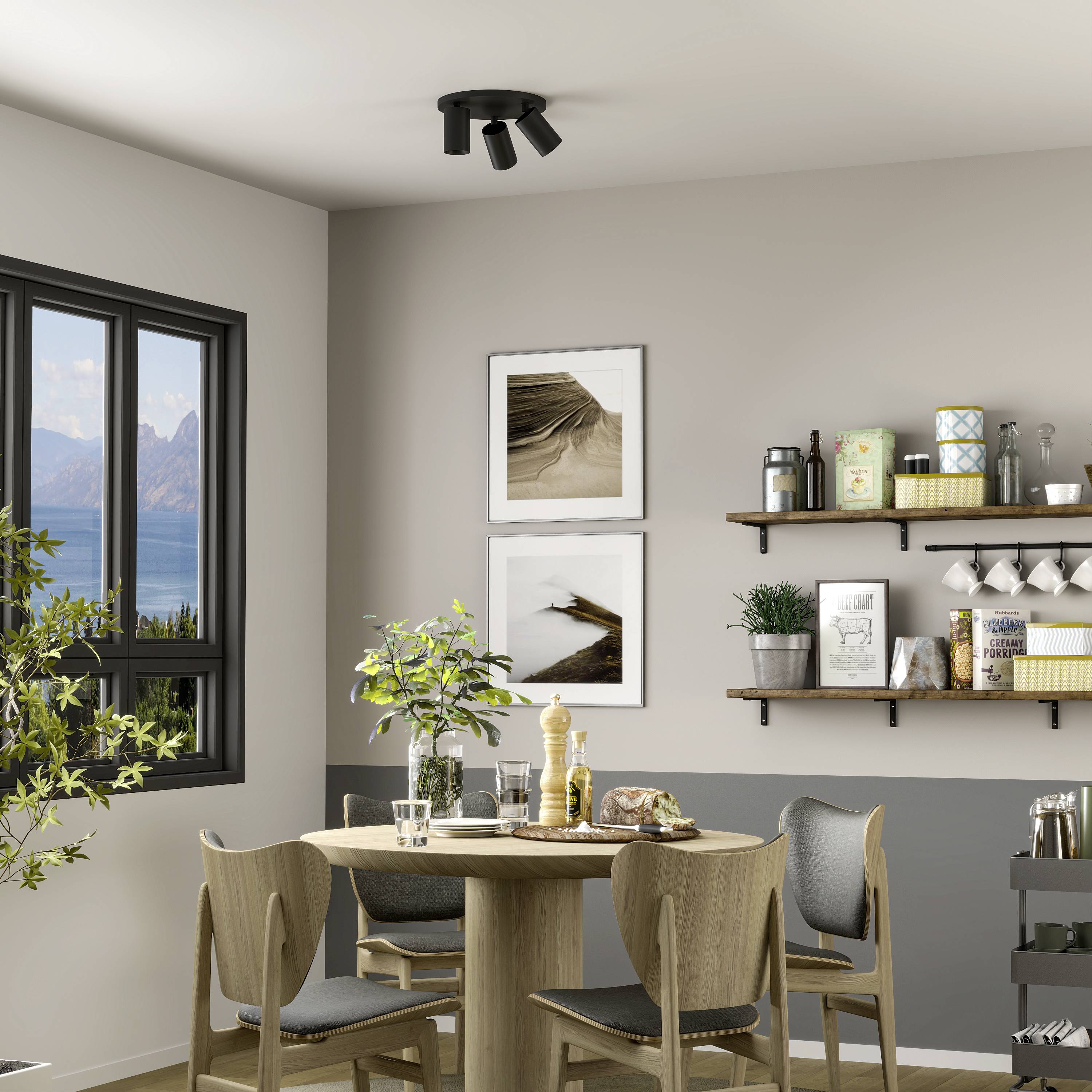 Jadalnia z okrągłym stołem i czterema krzesłami. Na stole stoi roślina, a półki i obrazy zdobią ściany. Duże okno ukazuje widok na góry.