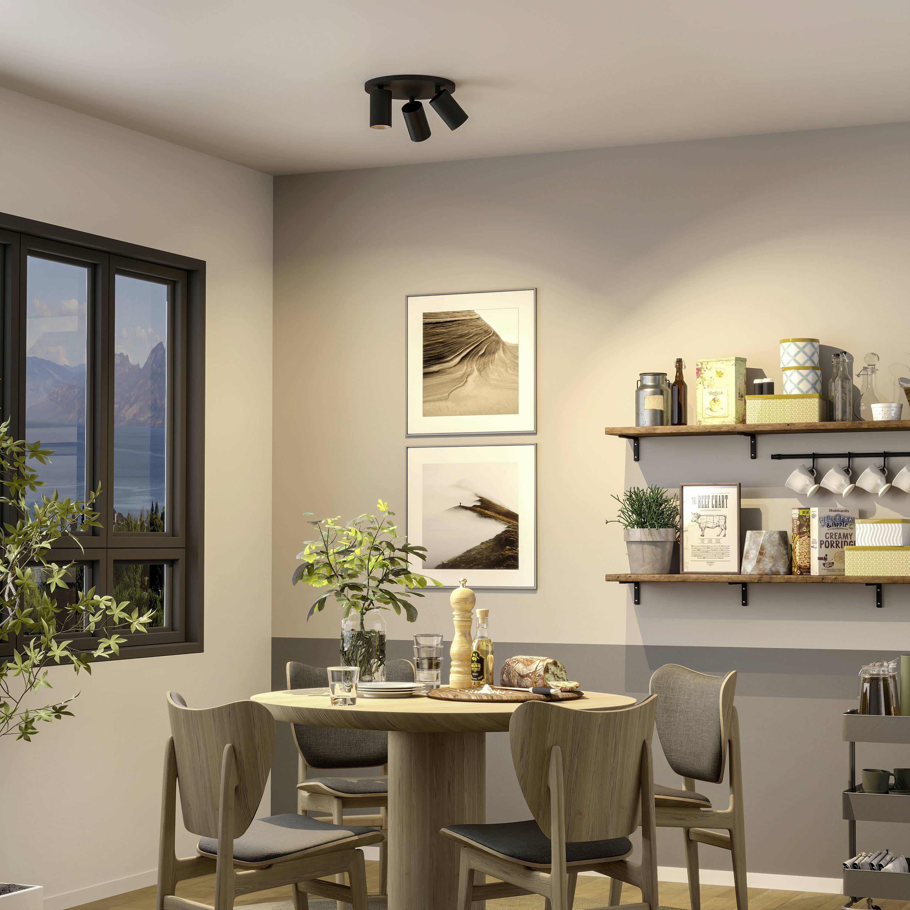 Jadalnia z okrągłym drewnianym stołem, czterema krzesłami, regałami z dekoracjami, roślinami i zdjęciami na ścianach. Okno z widokiem na góry.