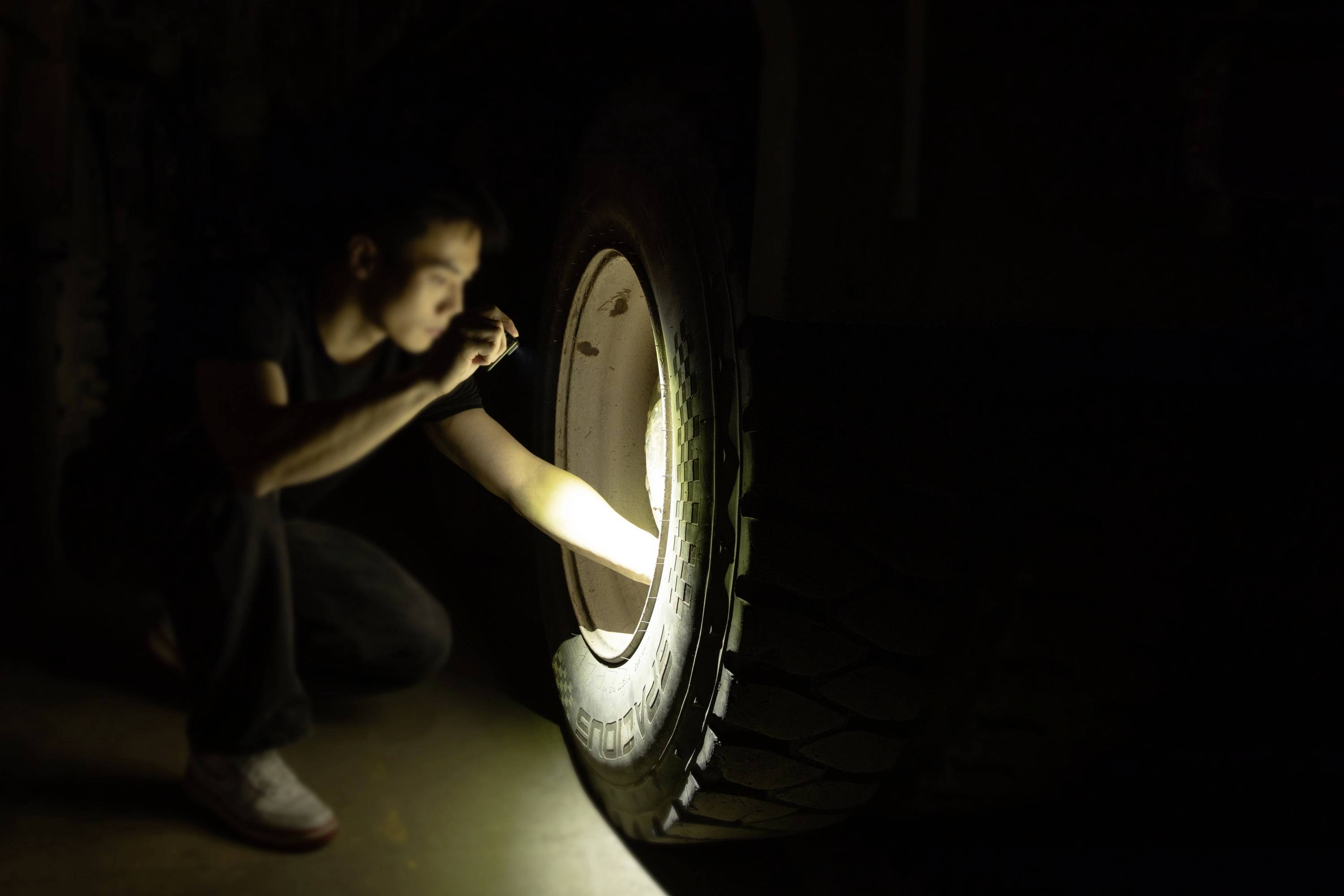 Osoba sprawdza latarką oponę dużego pojazdu w ciemnym otoczeniu.