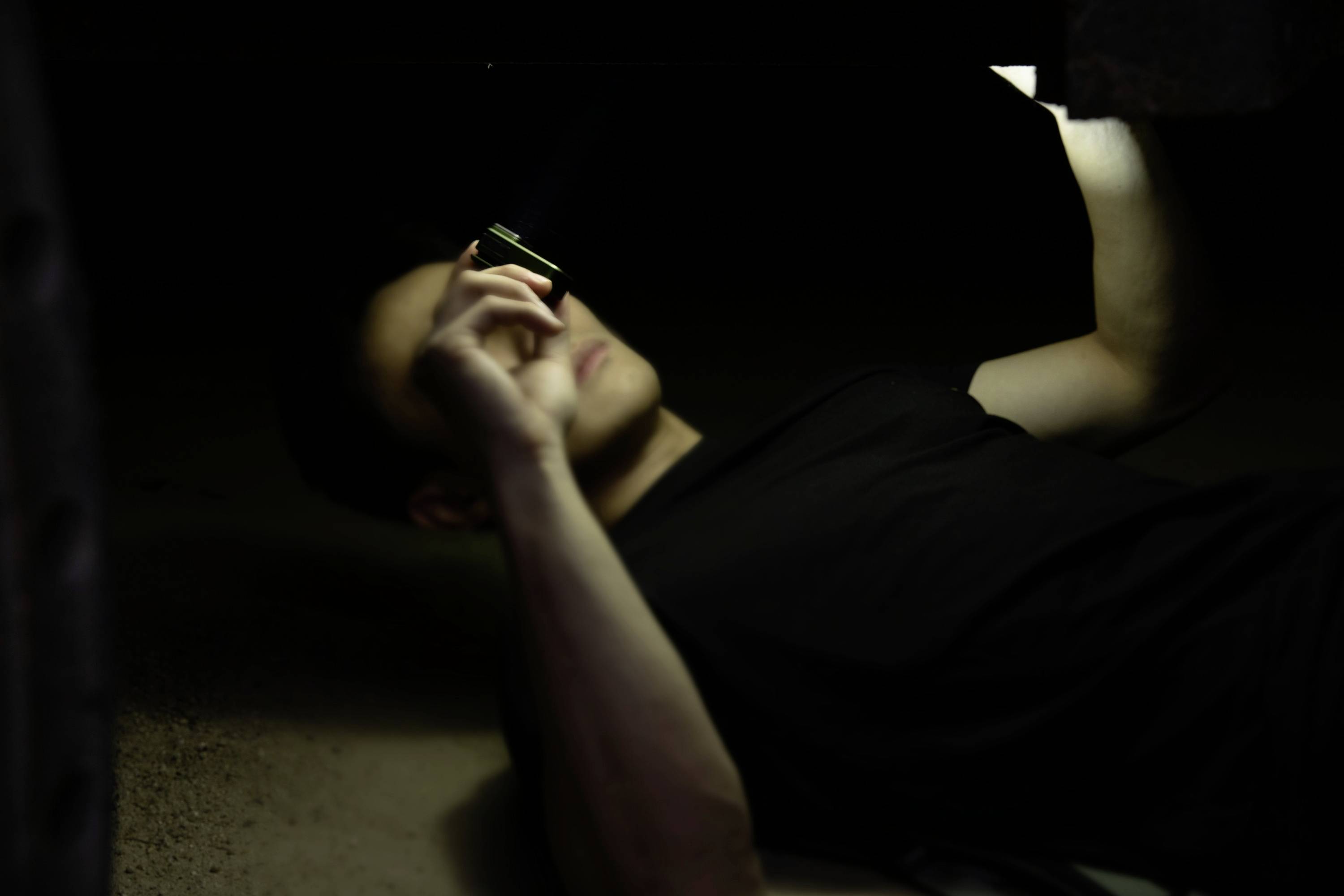 Osoba leży pod pojazdem i za pomocą latarki oświetla podwozie, aby wykonać naprawy lub przeprowadzić inspekcję.