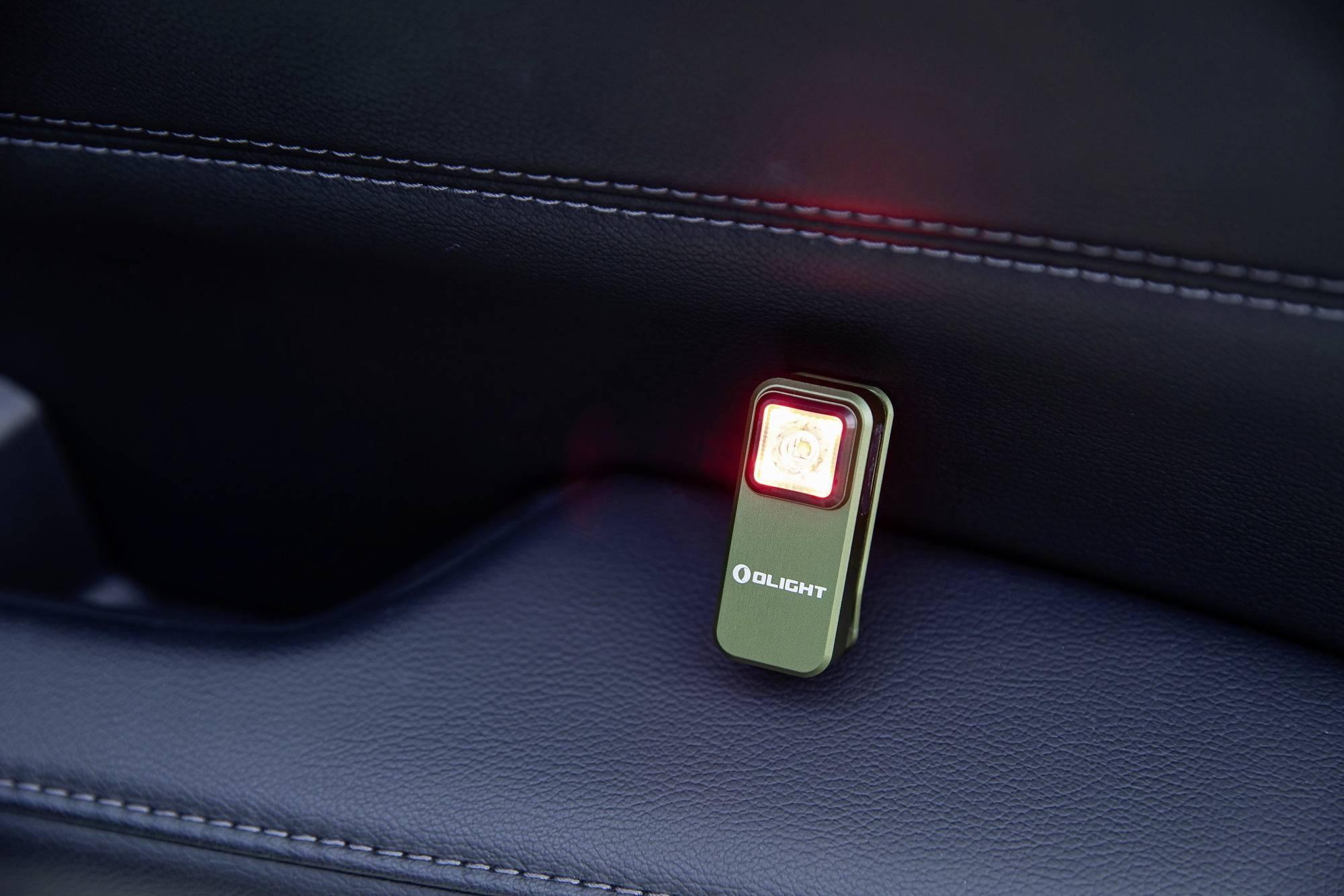 Mały, prostokątny przyrząd Olight ze świecącym czerwonym światłem znajduje się w pojeździe na ciemnej powierzchni.