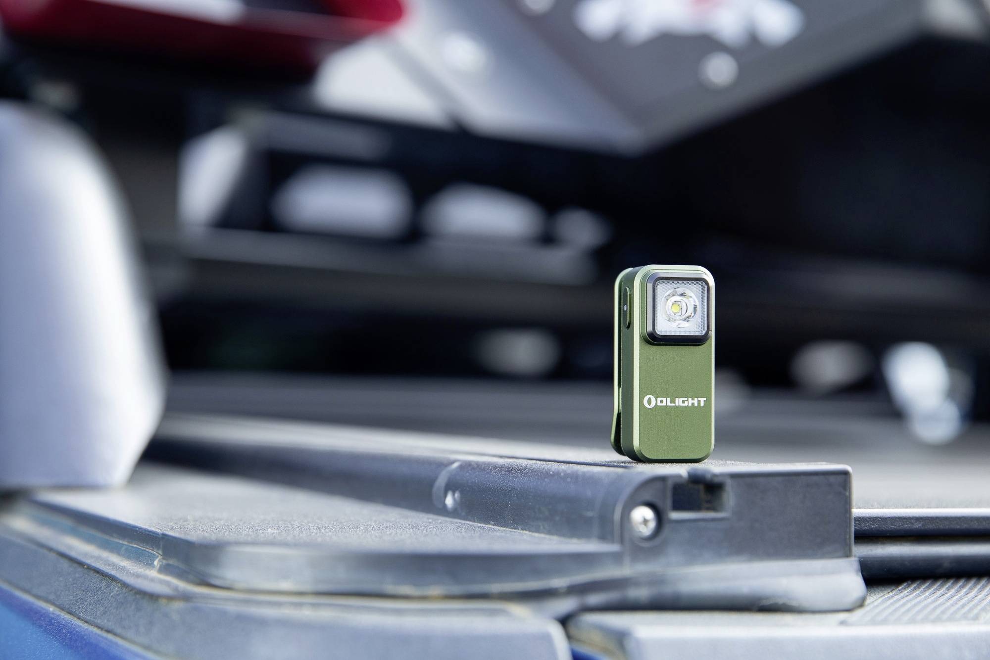Mały, zielony sześcian latarki kieszonkowej z logo marki, umieszczony na gładkiej powierzchni, z rozmytymi szczegółami pojazdu w tle.