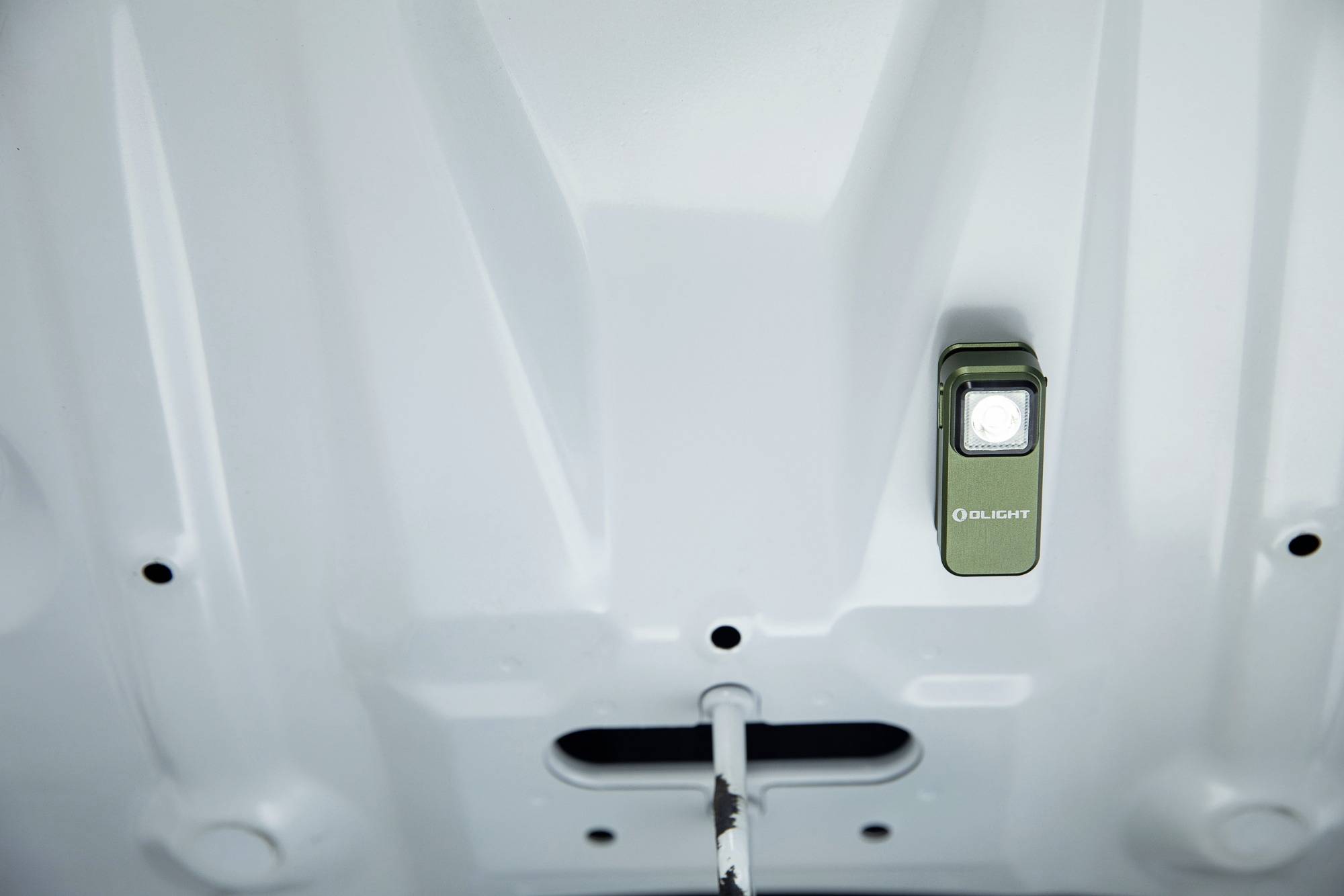 Zielona latarka świeci pod maską samochodu, oświetlając komorę silnika.