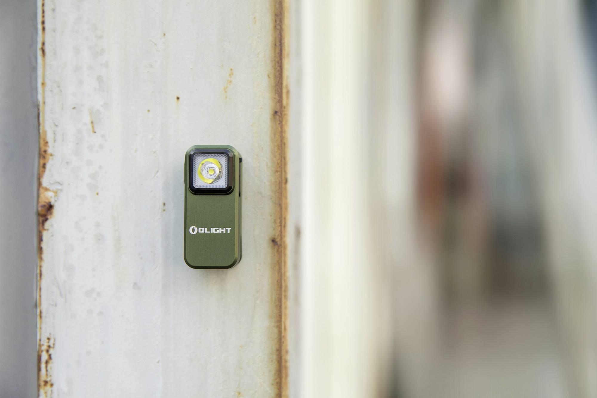 Mała, zielona latarka LED jest przymocowana do metalowej, lekko zardzewiałej powierzchni.