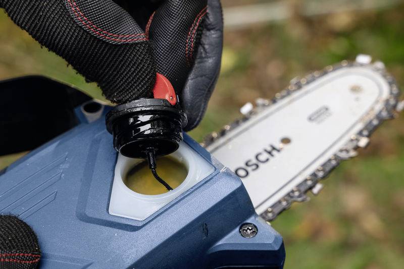 Osoba napełnia olejem elektryczną piłę łańcuchową. Widoczny jest łańcuch oraz obudowa piły.