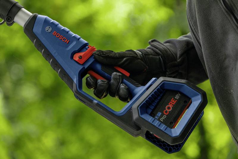 'Urządzenie akumulatorowe marki Bosch, trzymane przez osobę w czarnej rękawicy. Urządzenie jest niebieskie z czerwonymi akcentami, na wolnym powietrzu na zielonym tle.'