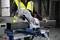 Osoba przecina metalową rurę piłą ukosową Bosch. Nosi żółtą kamizelkę ochronną w środowisku warsztatu.