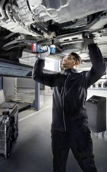 Mechanik naprawia pojazd za pomocą elektronarzędzia od spodu podniesinego samochodu w warsztacie samochodowym.