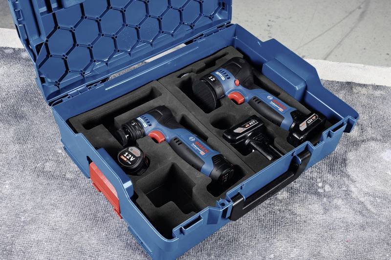 Niebieski kufer z narzędziami zawierający dwa niebieskie wkrętarki akumulatorowe i dwie baterie. Kufer jest otwarty i leży na szarym podłożu.