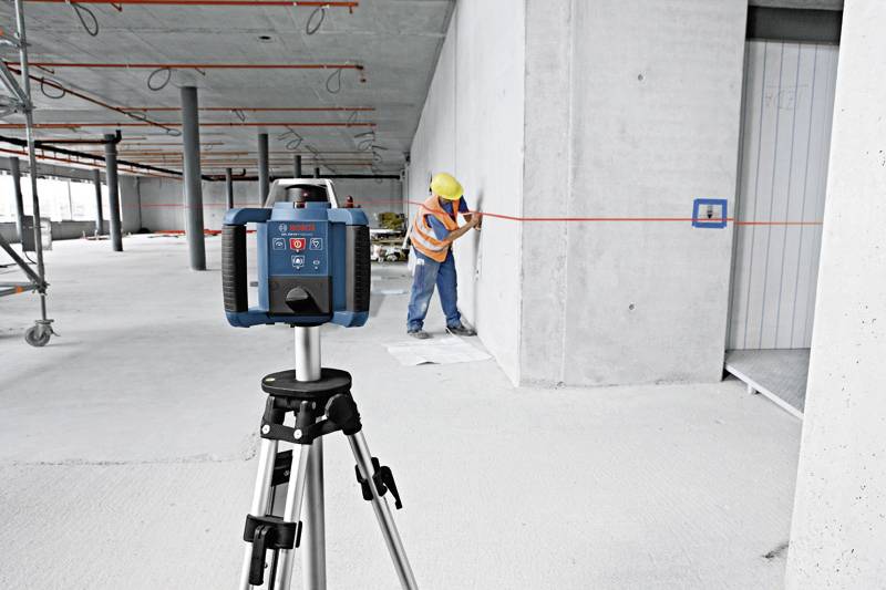 Robotnik w odzieży ochronnej sprawdza precyzję wykonania przy pomocy dalmierza laserowego w surowym budynku betonowym.