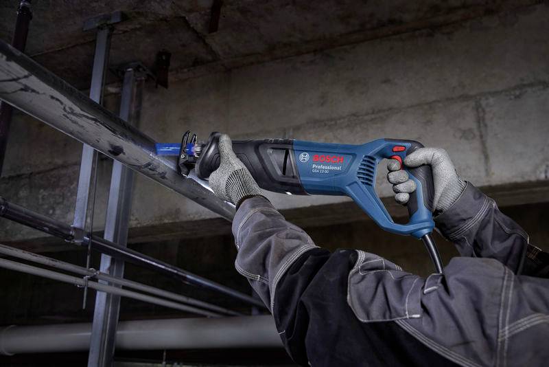 Osoba przecina metalową rurę niebieską wyrzynarką Bosch w przemysłowym otoczeniu. Precyzyjnie pracuje przy przewodzie rurowym.