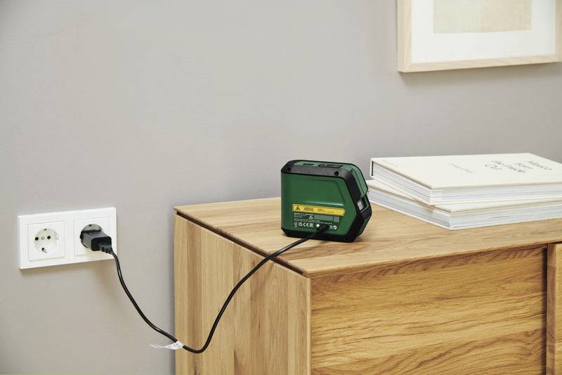 'Ładowarka jest podłączona do gniazdka elektrycznego, a urządzenie stoi na komodzie.'