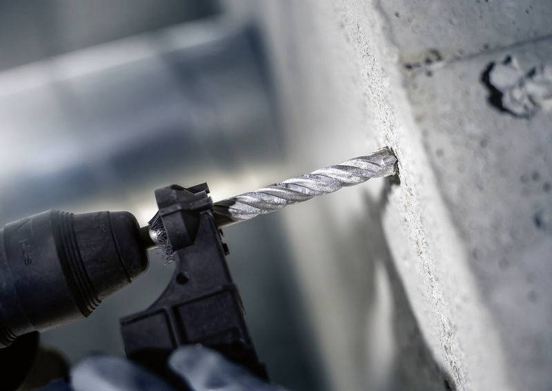 Osoba wywiera wiercenie wiertarką elektryczną w ścianę betonową. Wiertarka jest blisko obserwatora, a fokus spoczywa na miejscu wiercenia.