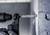 Wiertło przebija ścianę betonową, ujęcie z bliska. Wiertło jest w ruchu i wytwarza pył, który unosi się od ściany.