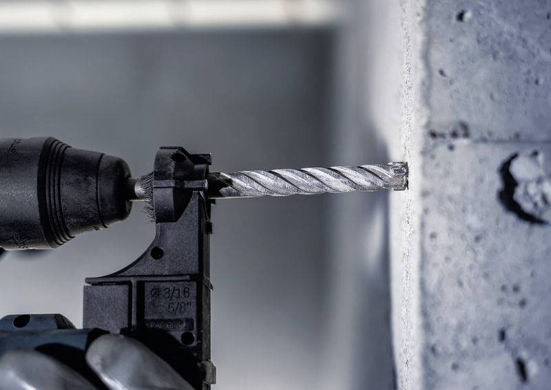 Elektryczny wiertarka, która wwierca się w szarą ścianę betonową. Czubek wiertła właśnie przebija powierzchnię.