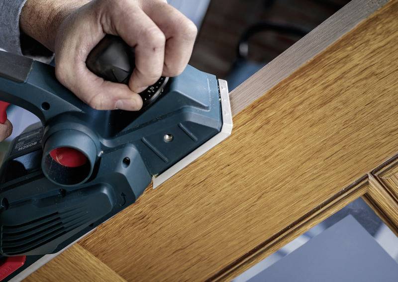 Osoba wyrównuje krawędź drewna elektrycznym strugarkiem.