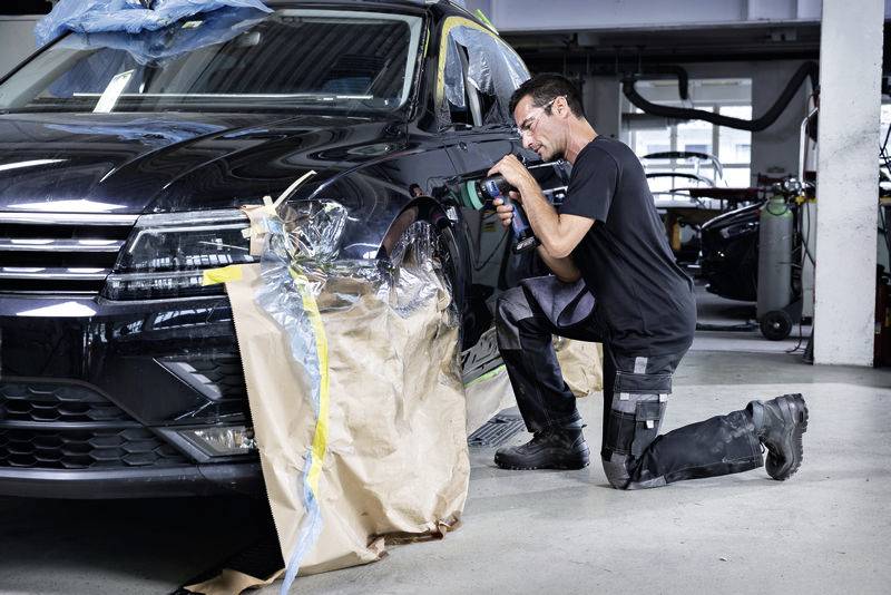 Mężczyzna klęczy obok czarnego samochodu i za pomocą narzędzia naprawia karoserię, aby poprawić lub naprawić lakier.