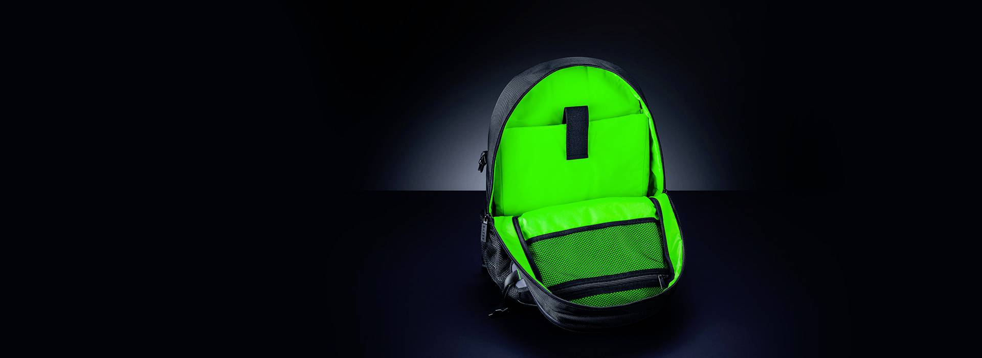 Plecak w jaskrawozielonym kolorze na ciemnym tle, otwarty z widocznymi przegródkami, oświetlony i będący w centrum uwagi.