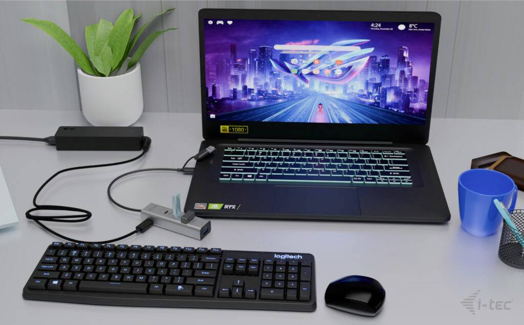 Laptop na biurku wyświetla futurystyczną panoramę miasta na ekranie. Obok niego klawiatura, mysz, rośliny i akcesoria.