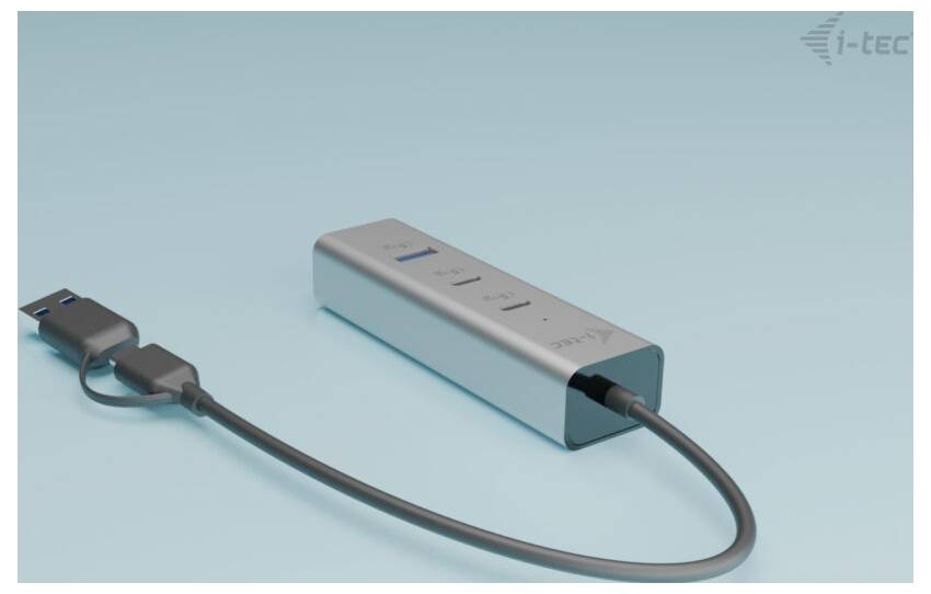 Srebrny hub USB z czterema portami, podłączony kablem USB, leży na jasnoniebieskiej powierzchni.