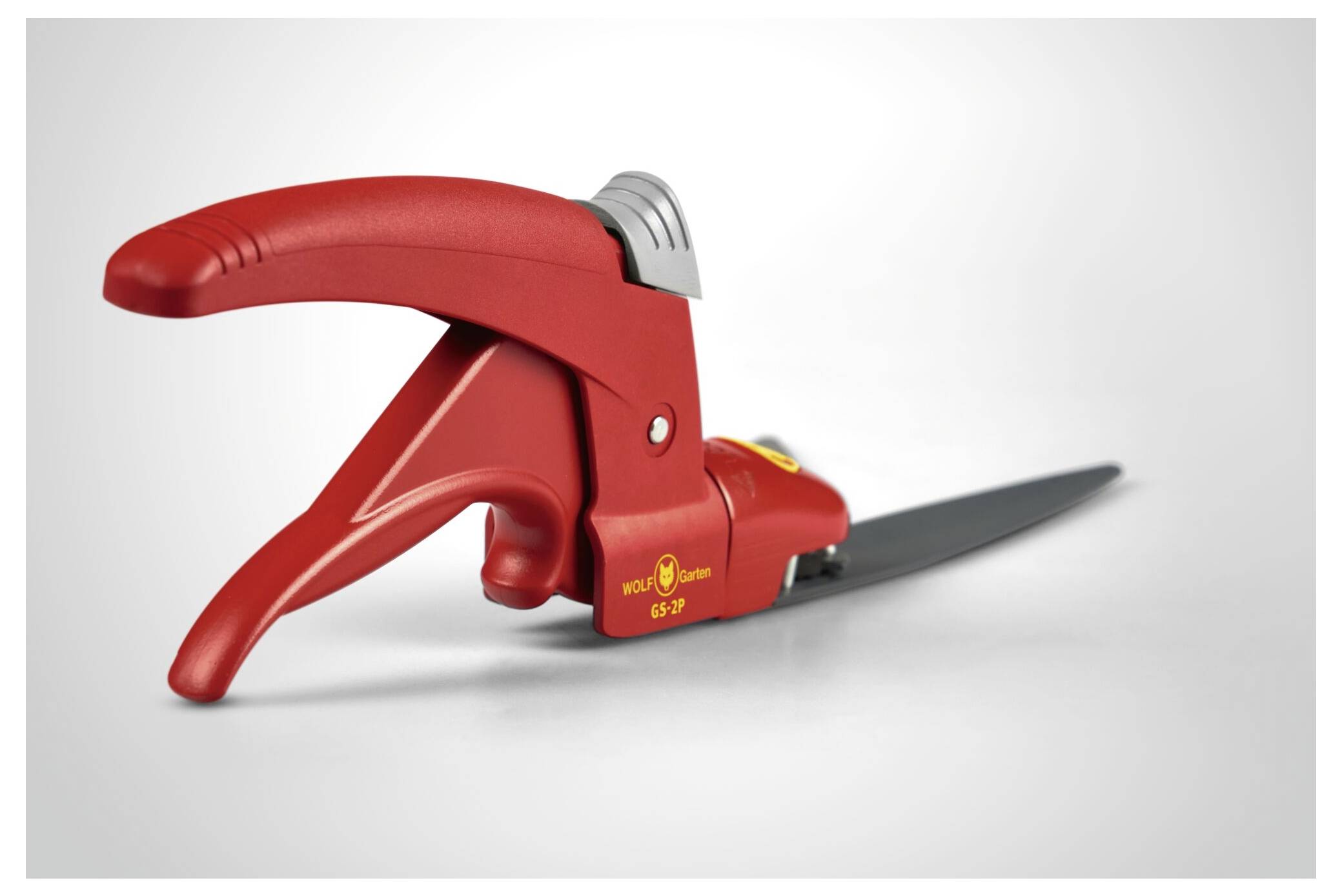 Czerwone nożyce do trawy z ergonomicznym uchwytem i srebrnym ostrzem, leżące na jasnym podłożu.