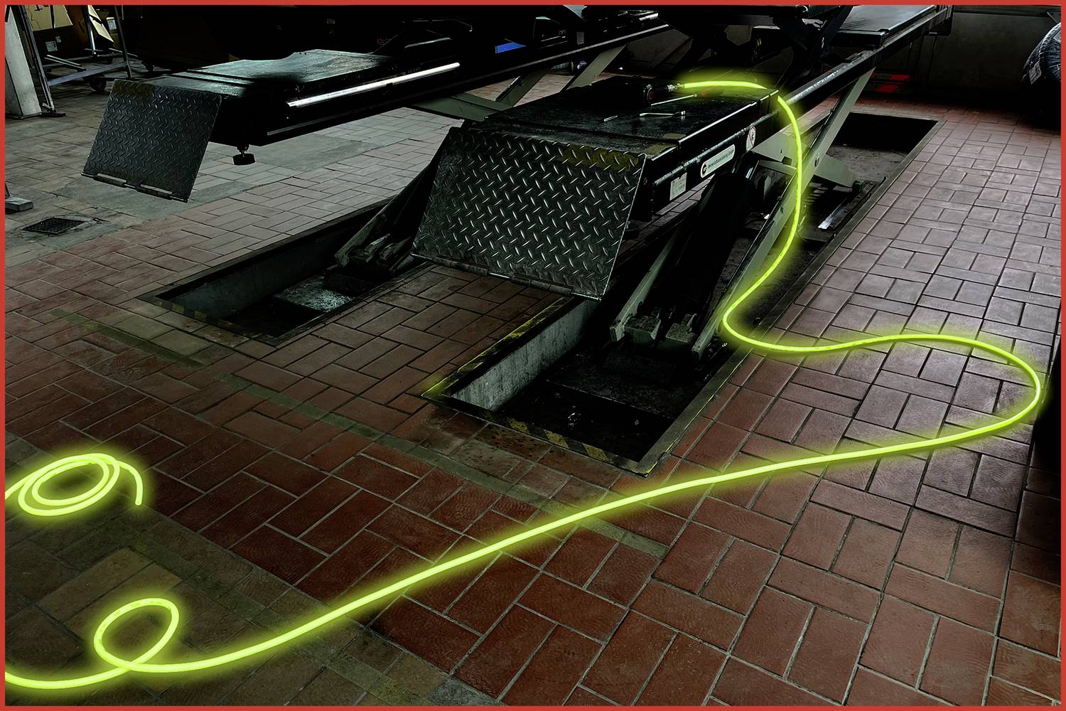 Warsztat samochodowy z podnośnikiem i jasno żółtym przewodem ułożonym na podłodze w dużym łuku.