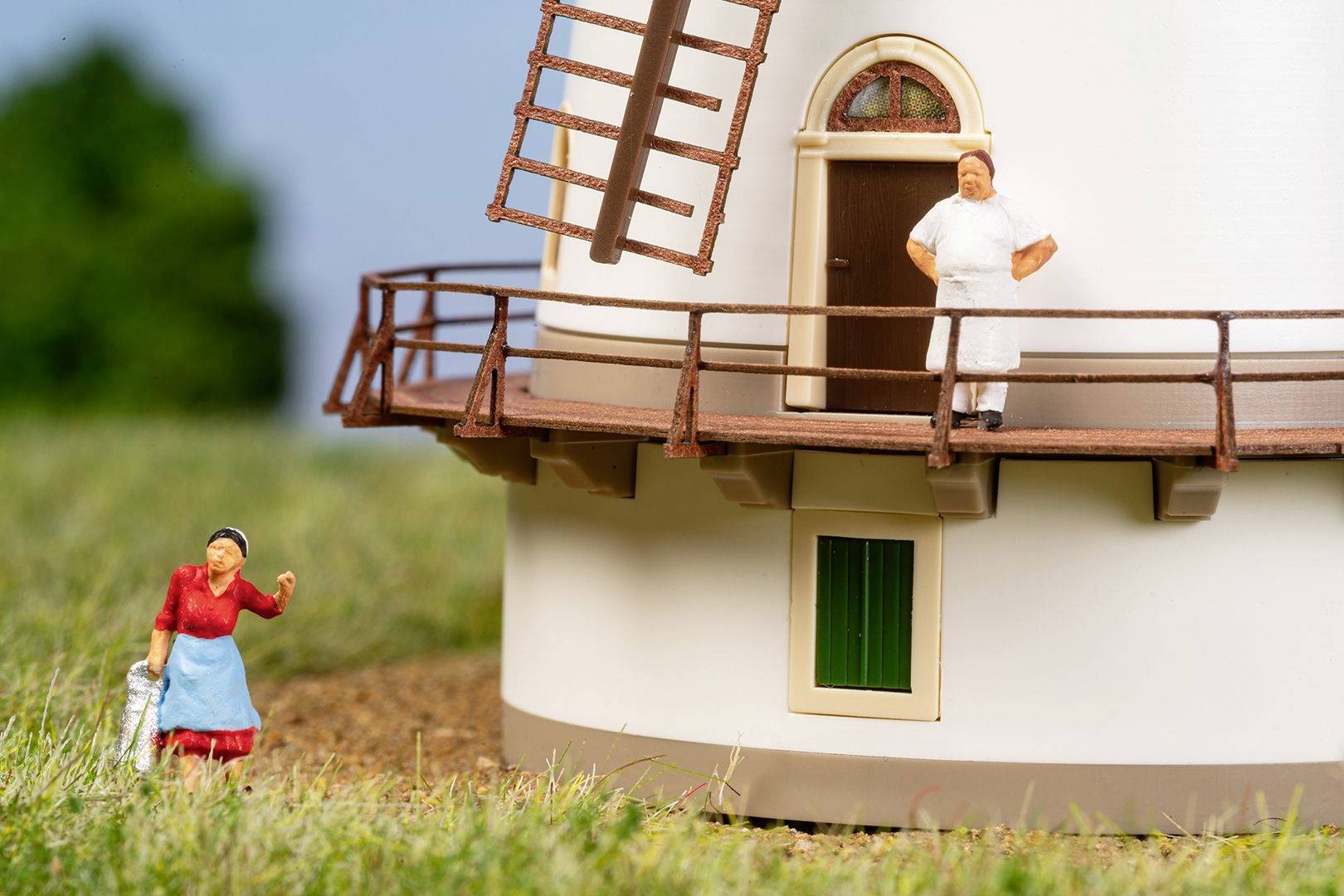 Miniaturowa makieta młyna piekarskiego z dwiema postaciami: piekarz stoi na balkonie, kobieta w czerwonej sukience patrzy w górę.
