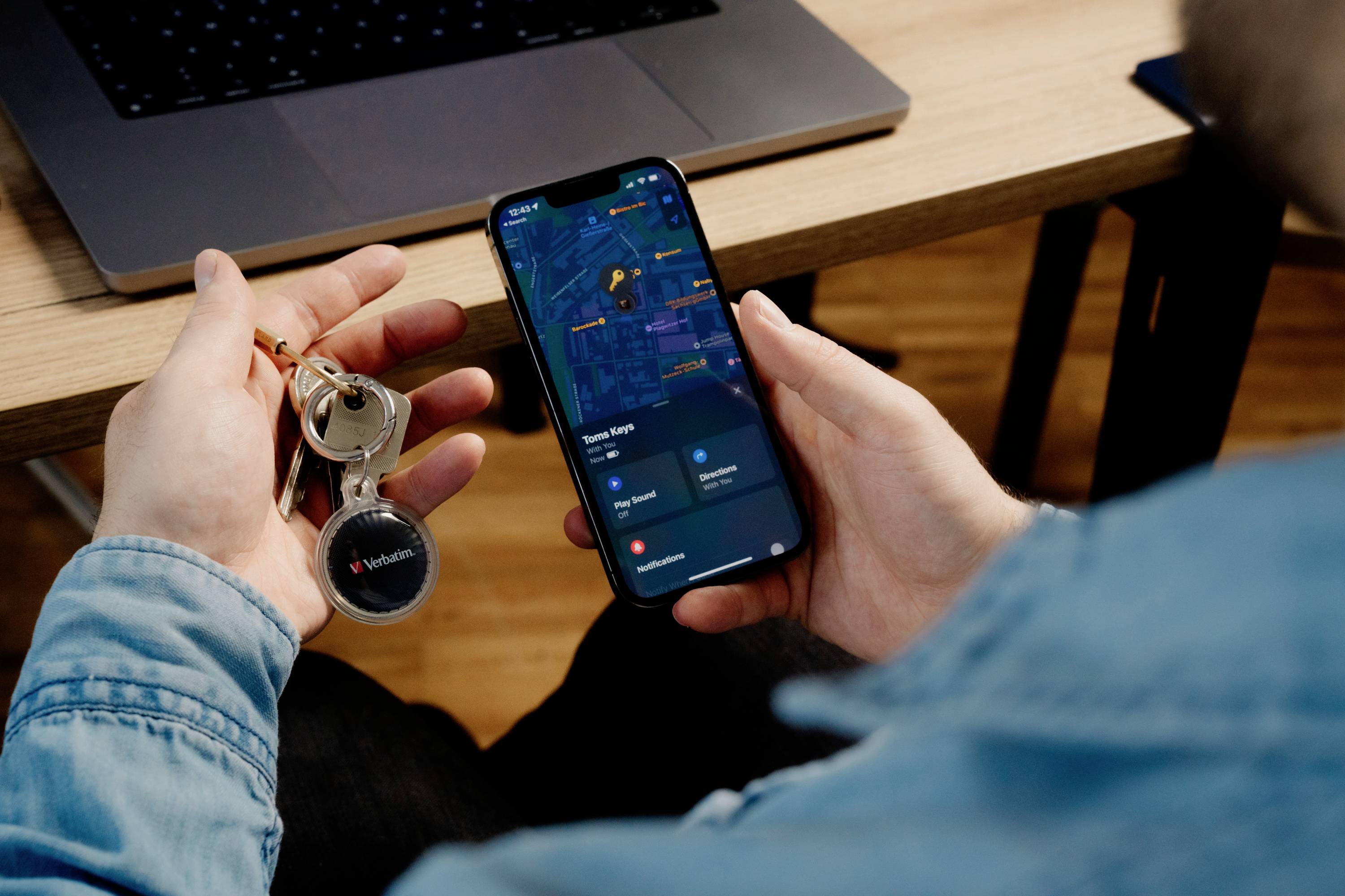 Osoba siedzi przed laptopem, trzymając w jednej ręce smartfona z otwartą aplikacją map, a w drugiej ręce klucze.