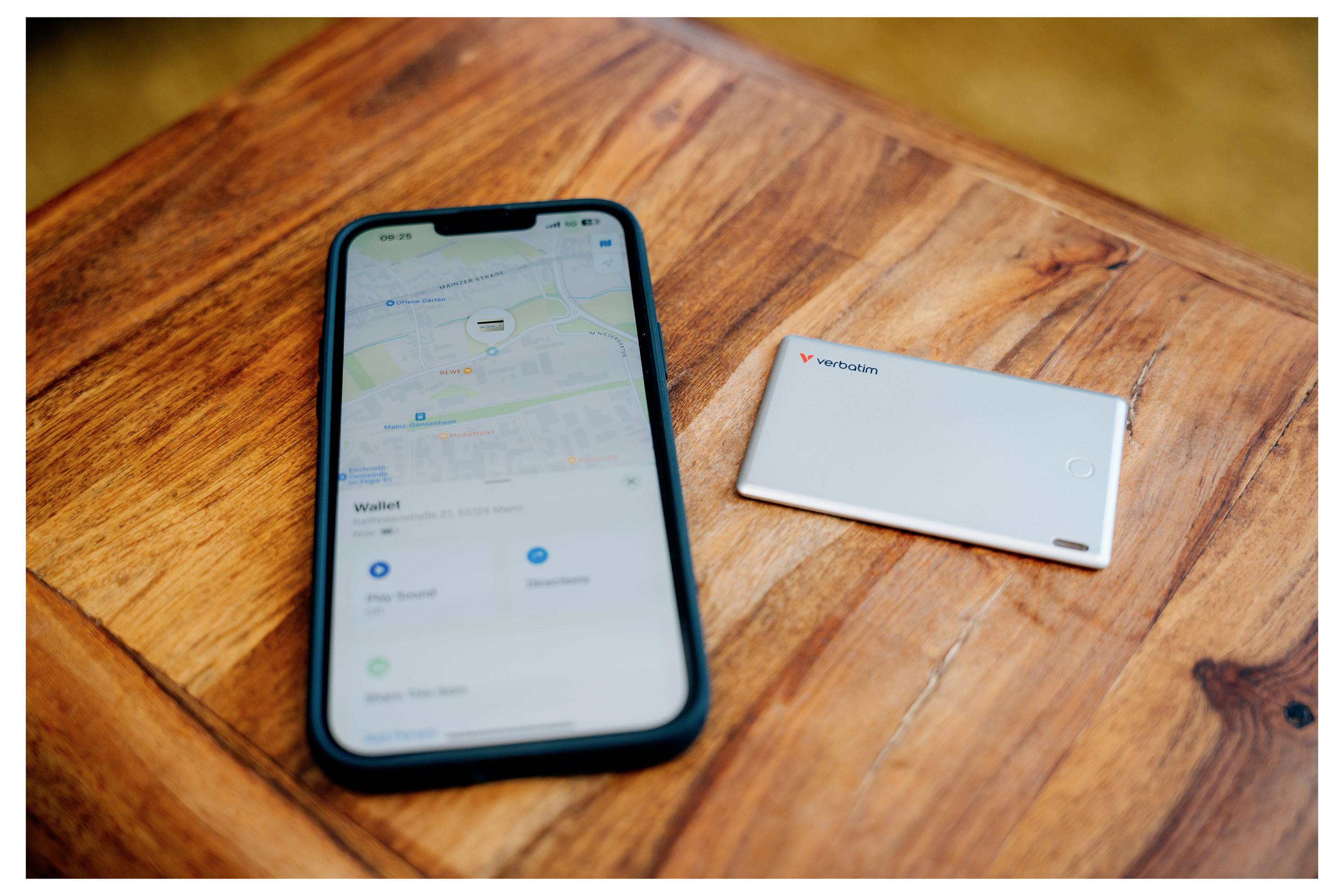 Smartfon z otwartą aplikacją map leży na drewnianym stole obok białego powerbanku.