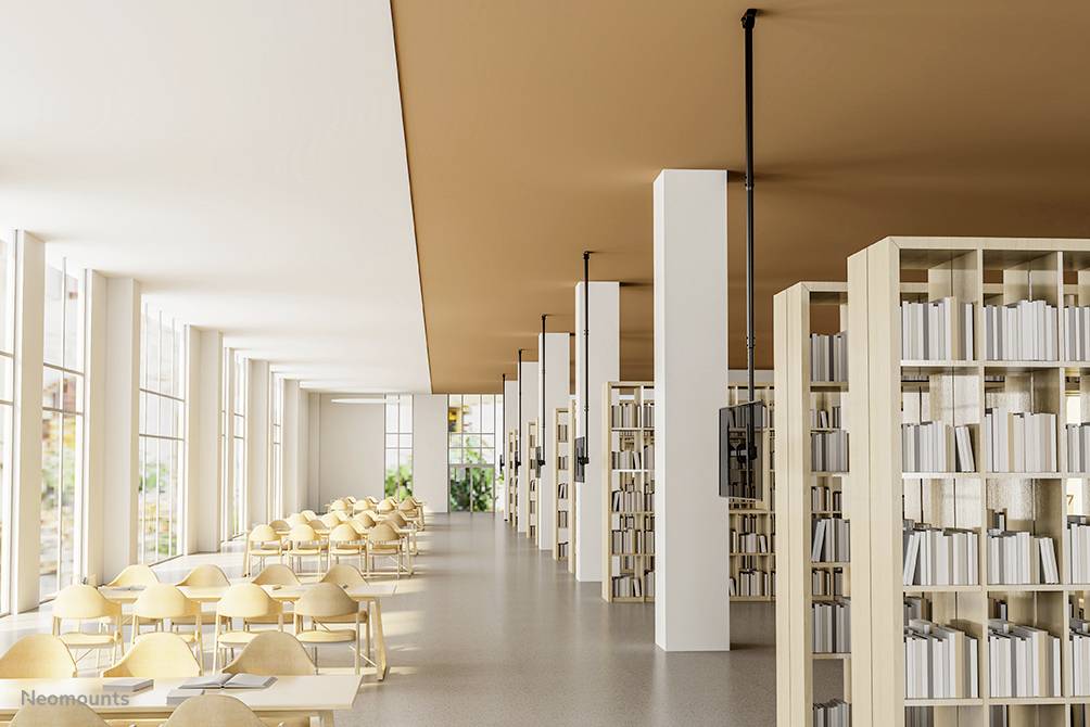 Jasne, nowoczesne pomieszczenie czytelni bibliotecznej z długimi stołami i regałami z książkami. Okna wpuszczają obficie światło dzienne.