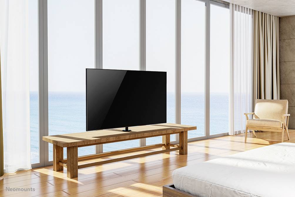 Telewizor stoi na drewnianym stoliku w nowoczesnym pokoju z dużymi oknami szklanymi i widokiem na morze.