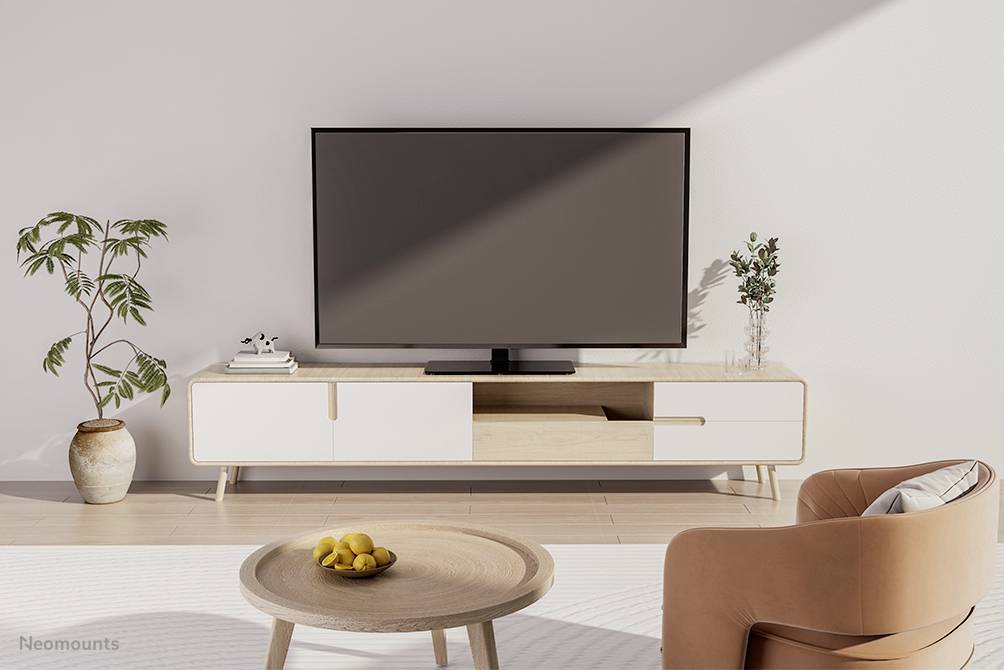 Nowoczesny salon z dużym telewizorem płaskim zamontowanym na szafce RTV w kolorze drewna i białej lakiery, obok której stoi zielona roślina. Na pierwszym planie znajduje się okrągły drewniany stolik z misą cytryn.