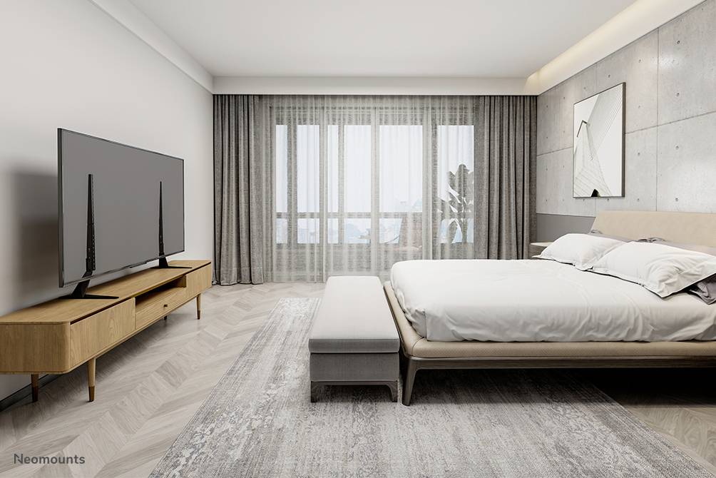 Nowoczesna sypialnia z dużym łóżkiem, drewnianym stolikiem pod telewizor z płaskim ekranem oraz dużym oknem zawieszonym zasłonami.