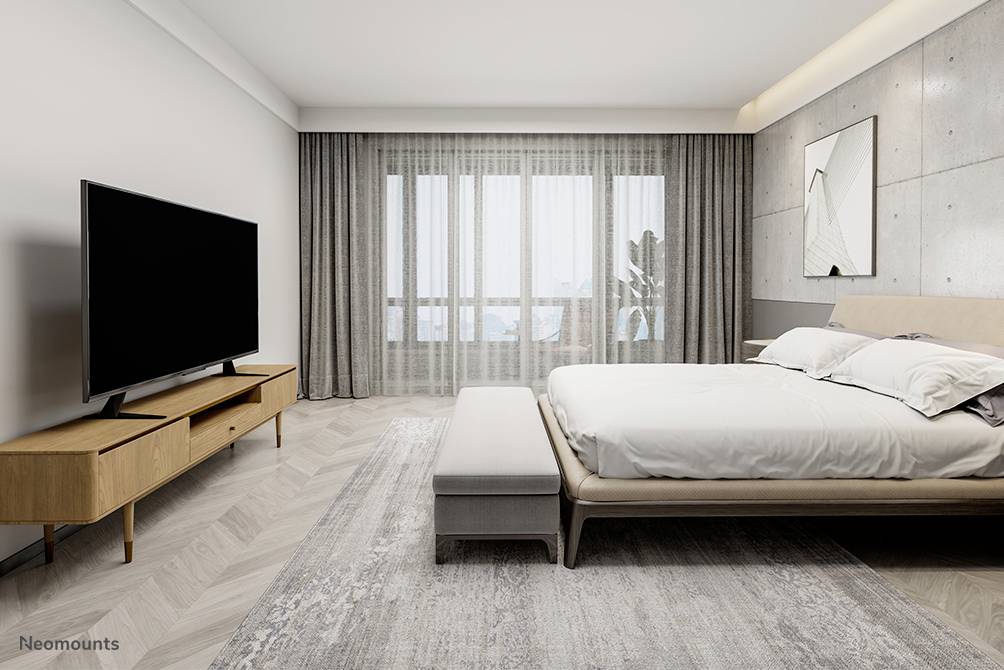 Sypialnia z dużym łóżkiem i telewizorem LCD na nowoczesnej drewnianej szafce. Duże okna z szarymi zasłonami, jasne ściany.