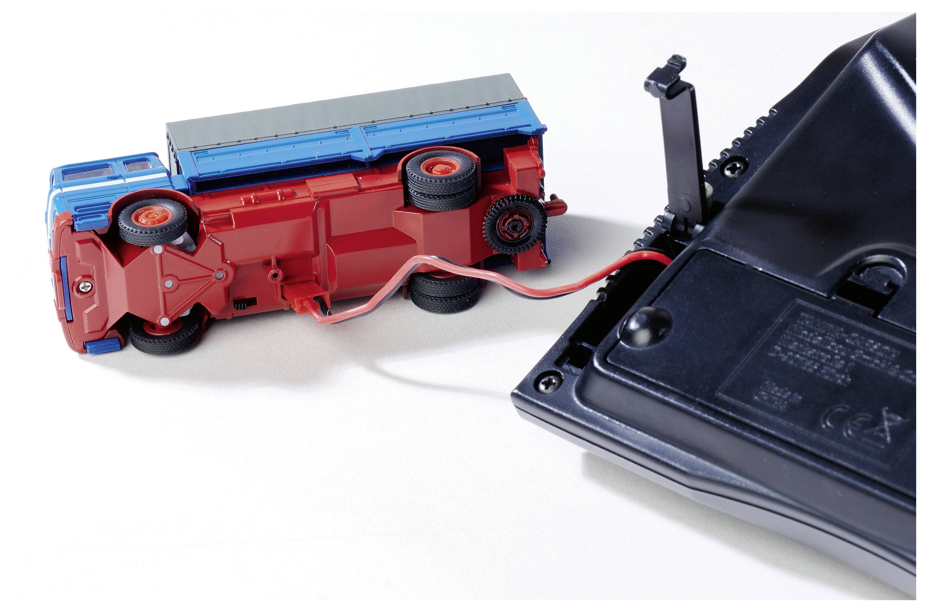 Przewrócony zabawkowy wóz strażacki jest podłączony do czarnego urządzenia. Czerwony kabel łączy te dwa obiekty.