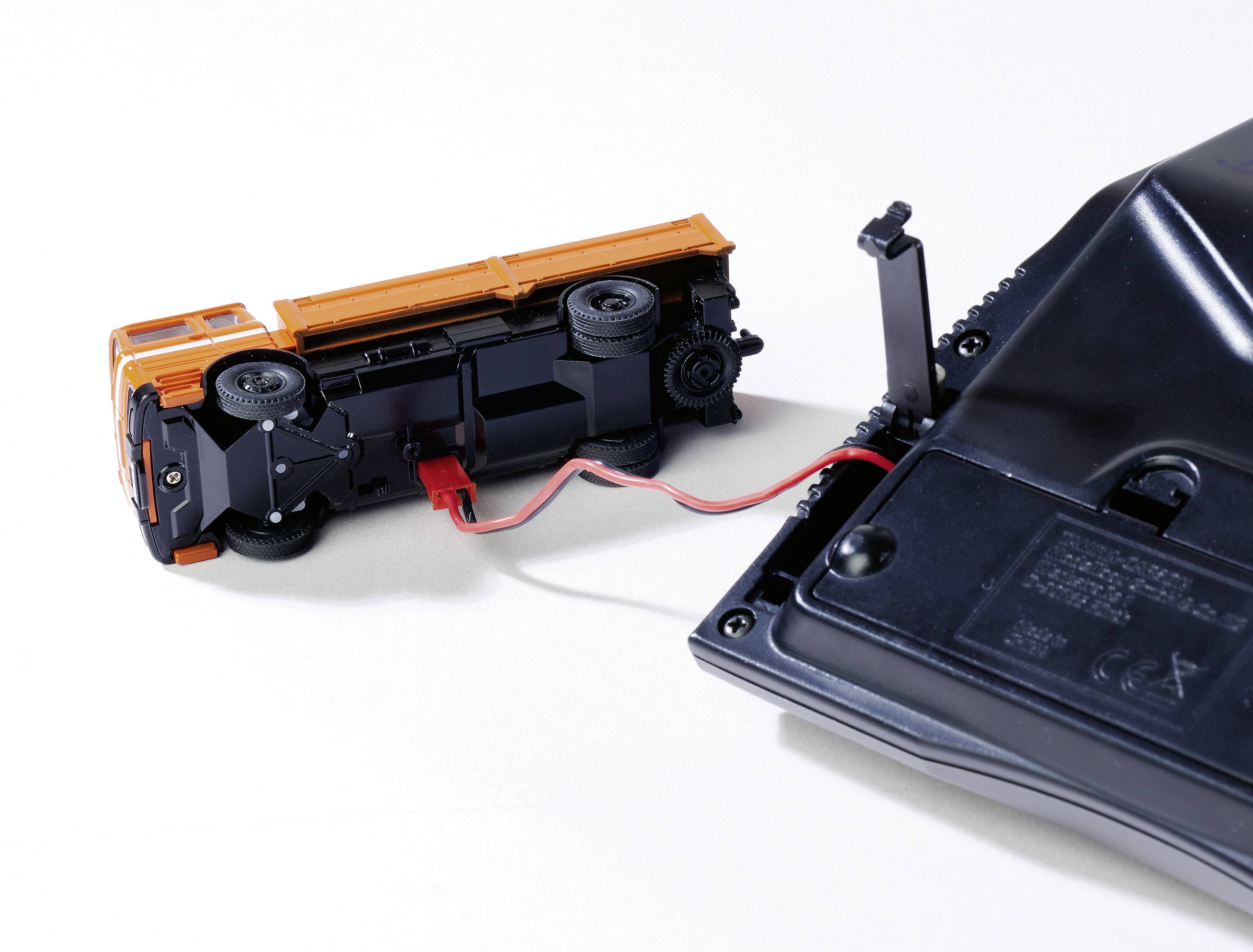 Zabawkowy samochodzik zdalnie sterowany. Samochód leży na boku, połączony przewodem z pilotem.